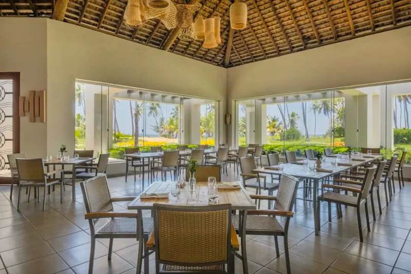 Salão de restaurante com mesas postas e grandes janelas para o jardim