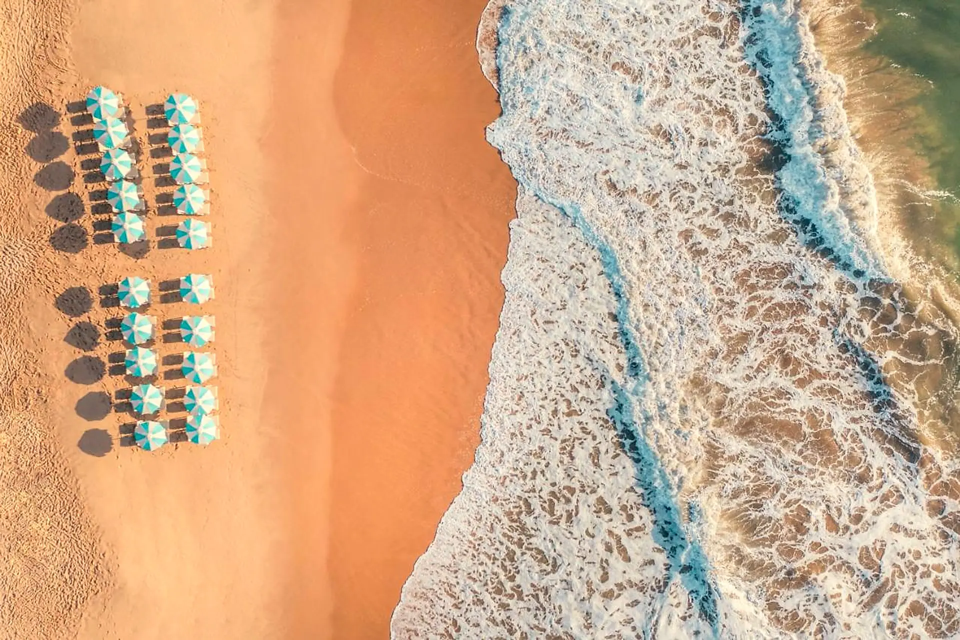 Vista aérea da praia com guarda-sóis e espreguiçadeiras na areia e as ondas do mar